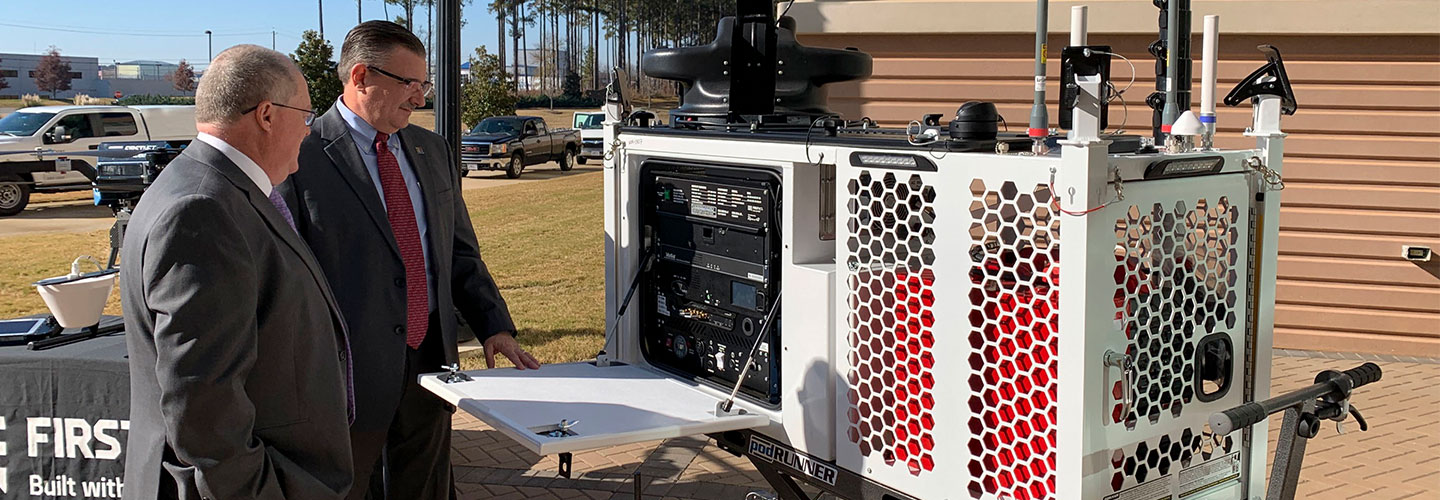 Two men stand beside a FirstNet Compact Rapid Deployable.