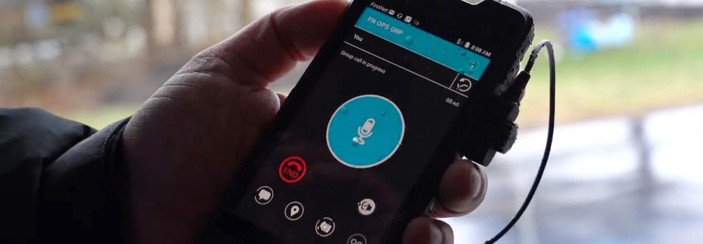 A first responder holds a smartphone showing a push-to-talk application